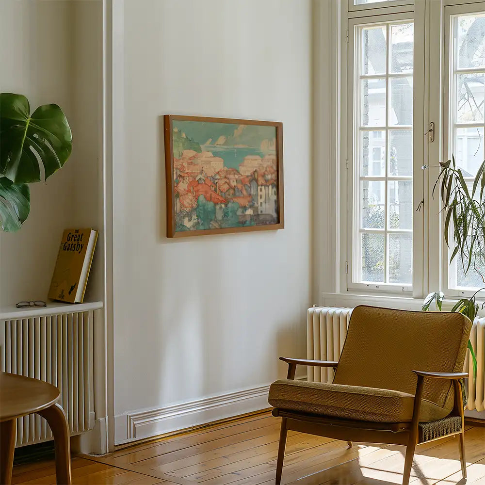 Framed painting of a coastal village with colorful rooftops, displayed on a light wall in a cozy living room setting.