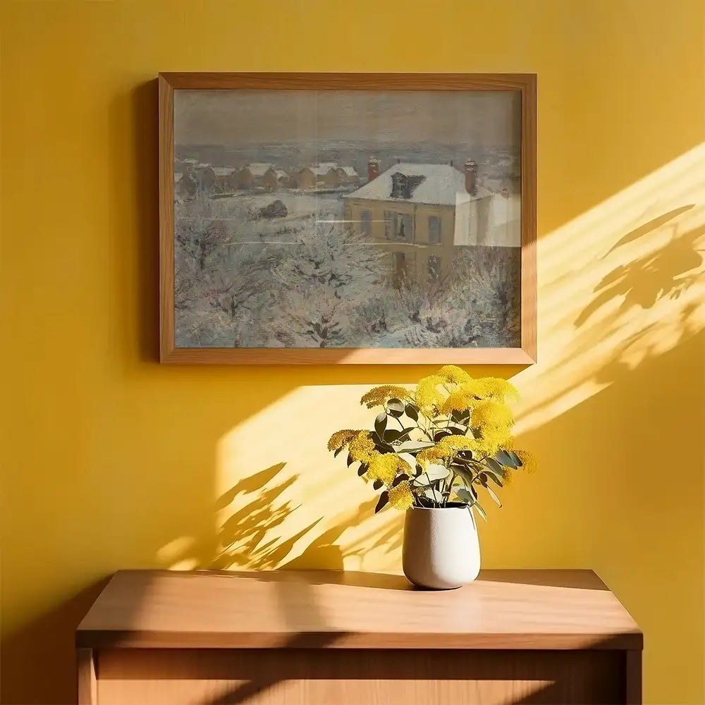 Framed painting of a winter landscape hanging on a yellow wall, with a vase of yellow flowers on a wooden table in the foreground.