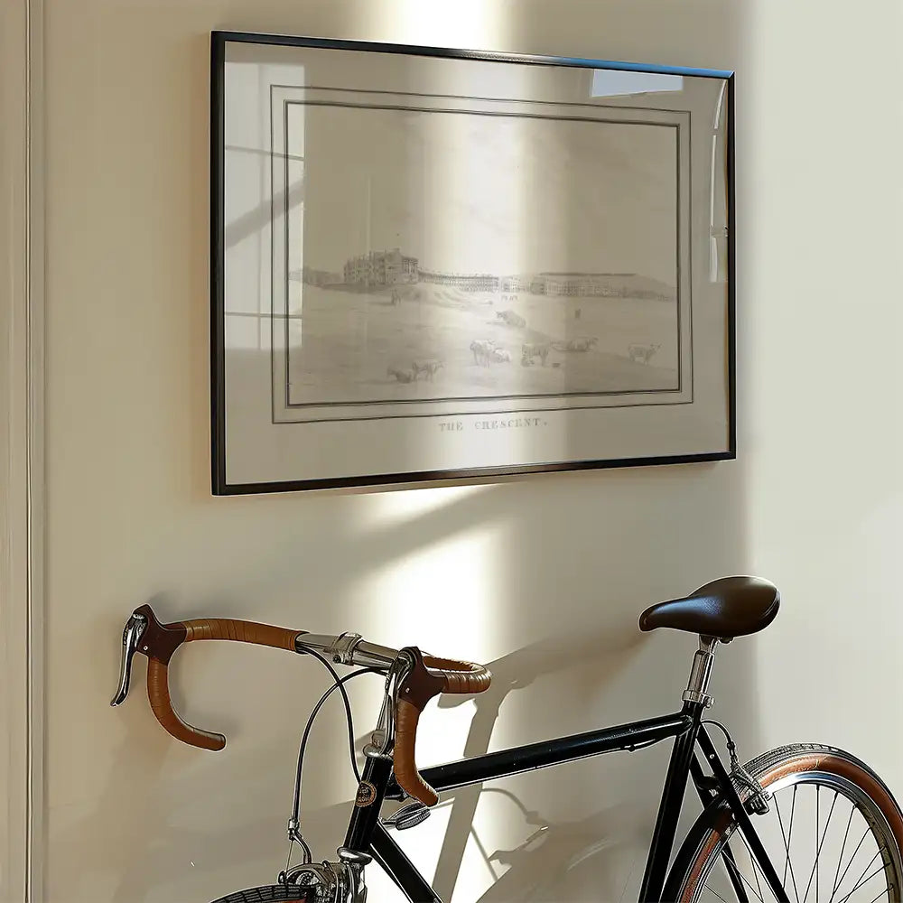 Framed vintage artwork titled "The Crescent" displayed on a wall with a bicycle leaning against it.