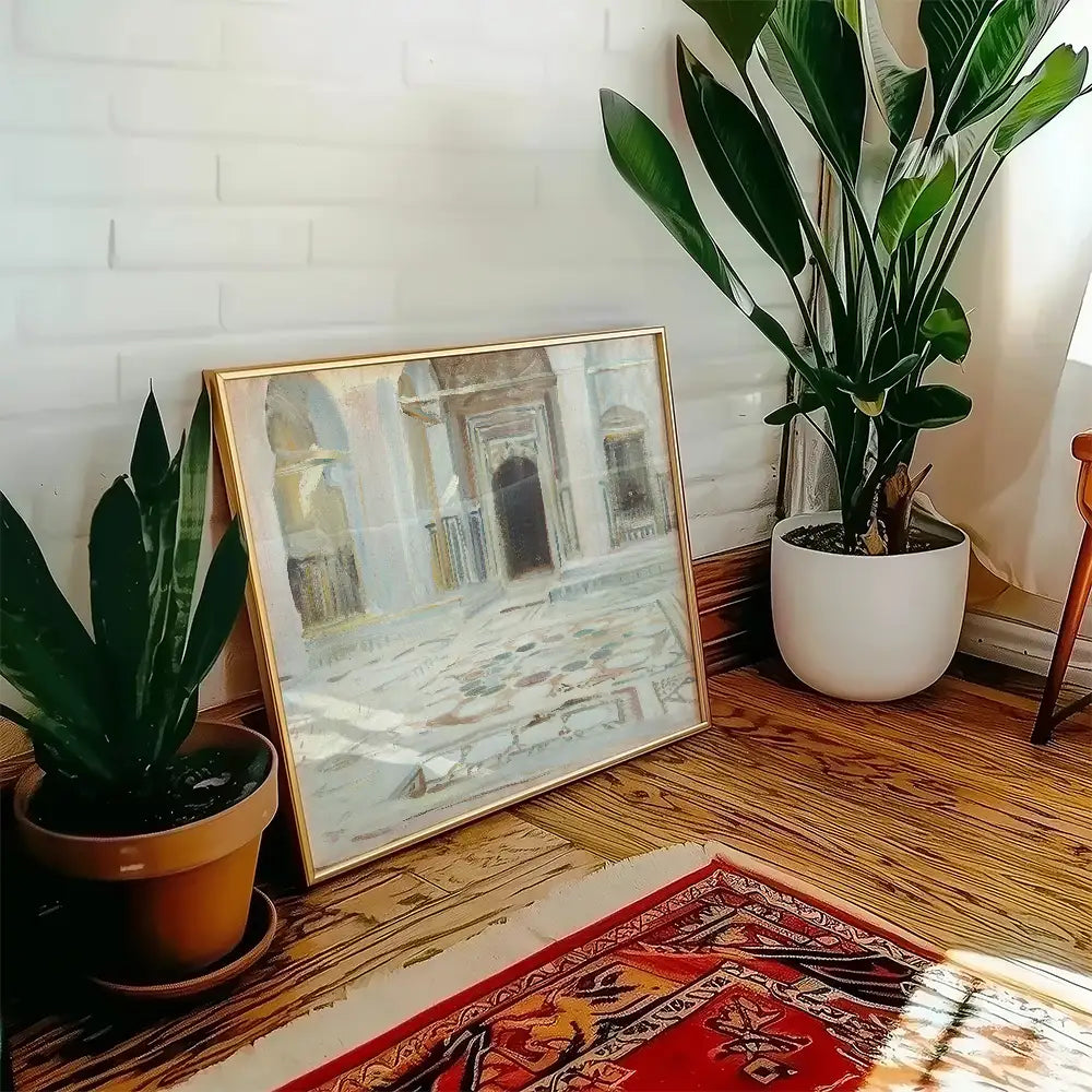 Painting in a gold frame leaning against a wall next to potted plants and a colorful rug.