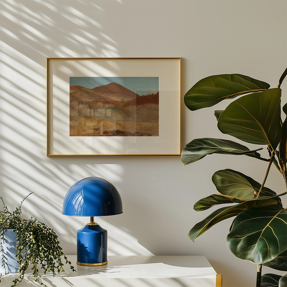 Framed landscape painting with mountains and hills hanging on a wall next to a blue lamp and a green plant.