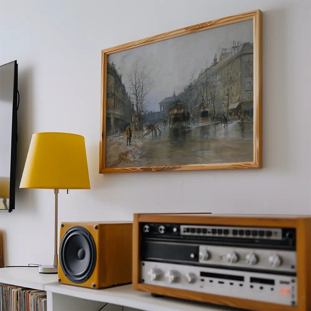 Painting of a city street scene framed and hung on a wall, with a yellow lamp and a retro audio system nearby.