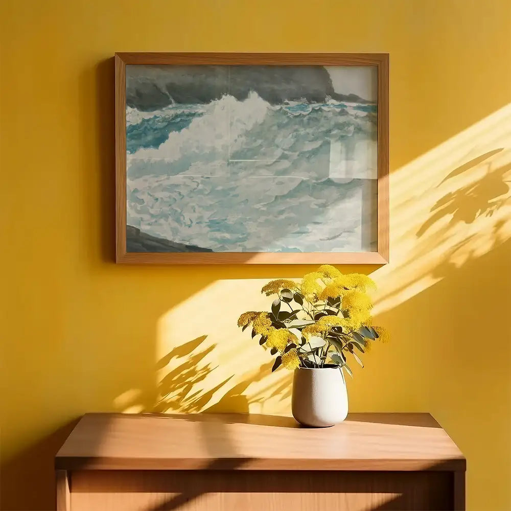 Framed painting of ocean waves on a bright yellow wall with a vase of yellow flowers on a wooden table.
