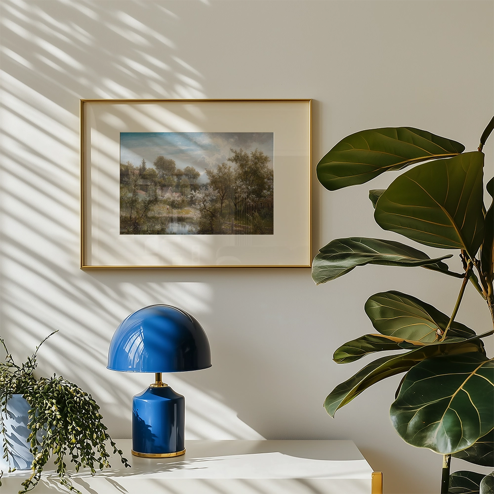 Framed painting of a serene landscape featuring trees and a body of water, displayed on a wall beside a blue lamp and greenery.