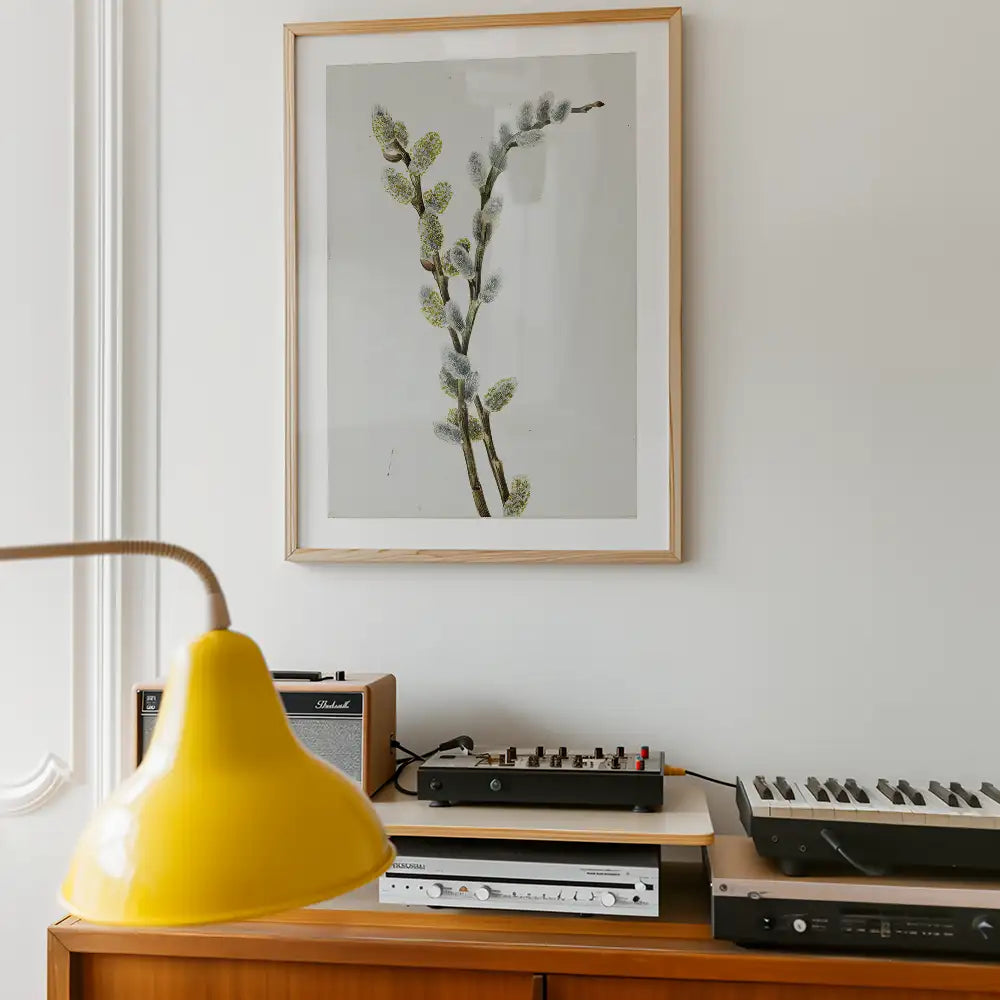 Framed botanical print of pussy willow branches on a wall above a wooden table with various audio equipment and a yellow lamp.