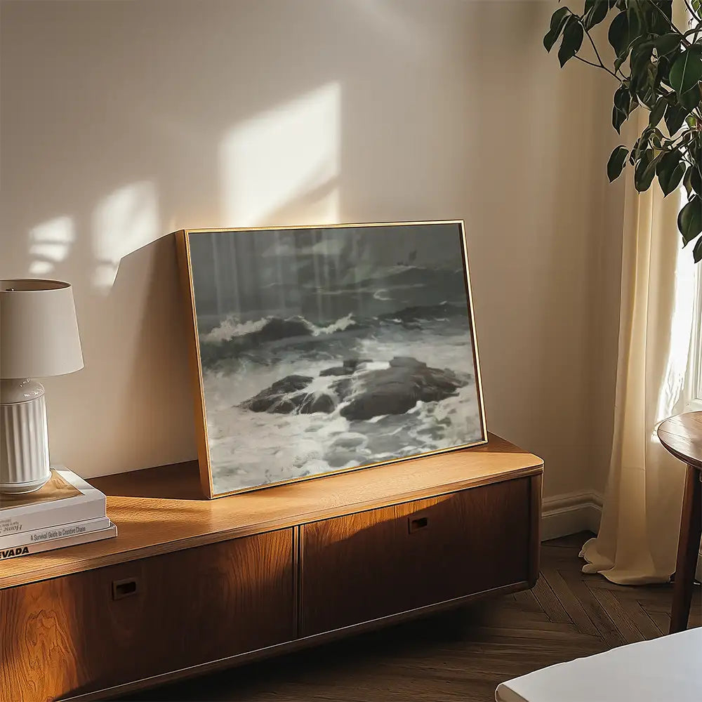 Framed painting of crashing waves against rocks displayed on a wooden console table in a bright, modern living room.