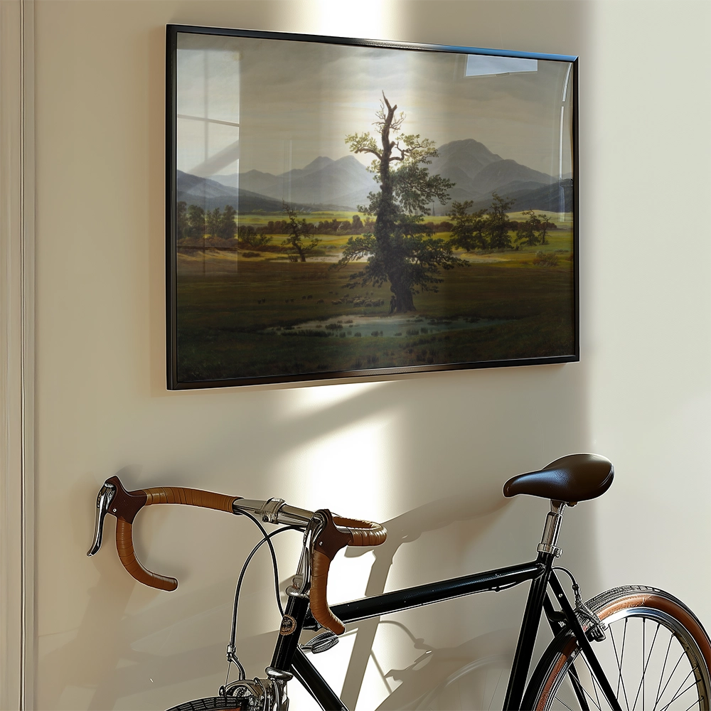 Framed landscape painting depicting a tree and mountains, displayed on a wall next to a black bicycle.