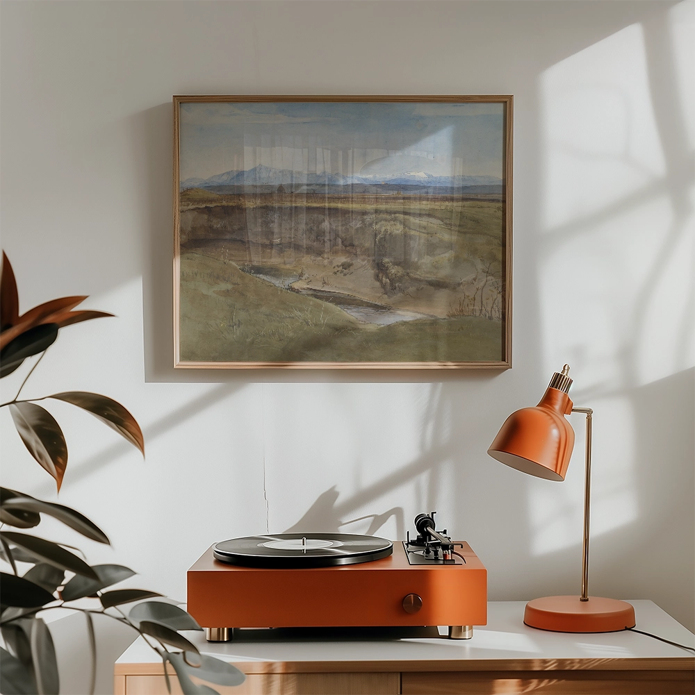 Framed painting of a serene landscape with mountains and a river, displayed above an orange turntable and lamp in a bright room setting.