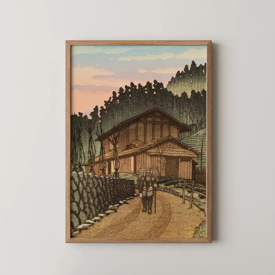 Framed painting of a rustic house and two hikers along a winding road, set against a colorful sunset sky and forest backdrop.
