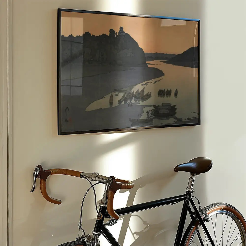 Framed painting of a serene river scene with boats and a distant hill, hanging on a wall beside a vintage bicycle.