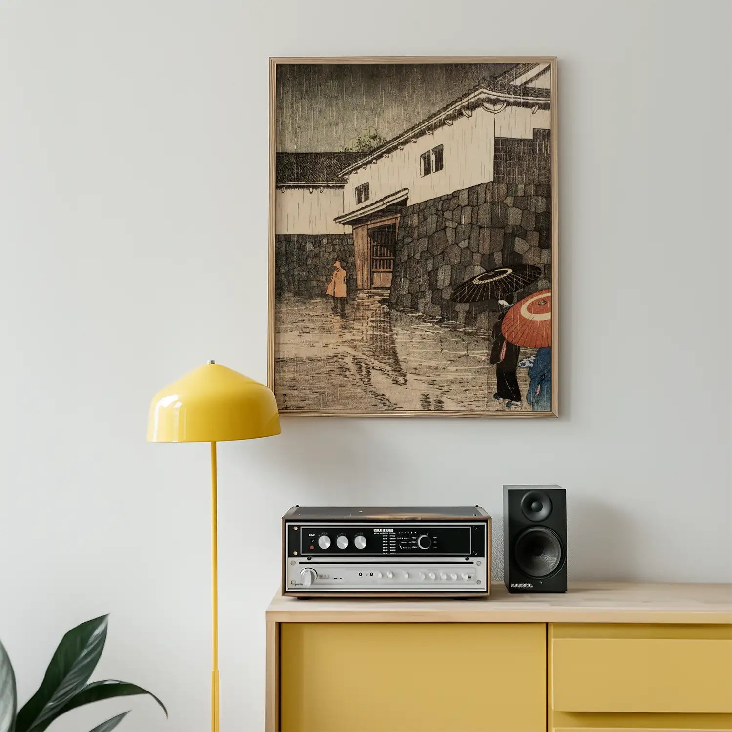 Framed painting of a rainy scene with figures holding umbrellas, displayed on a wall next to a yellow lamp and a vintage audio setup.