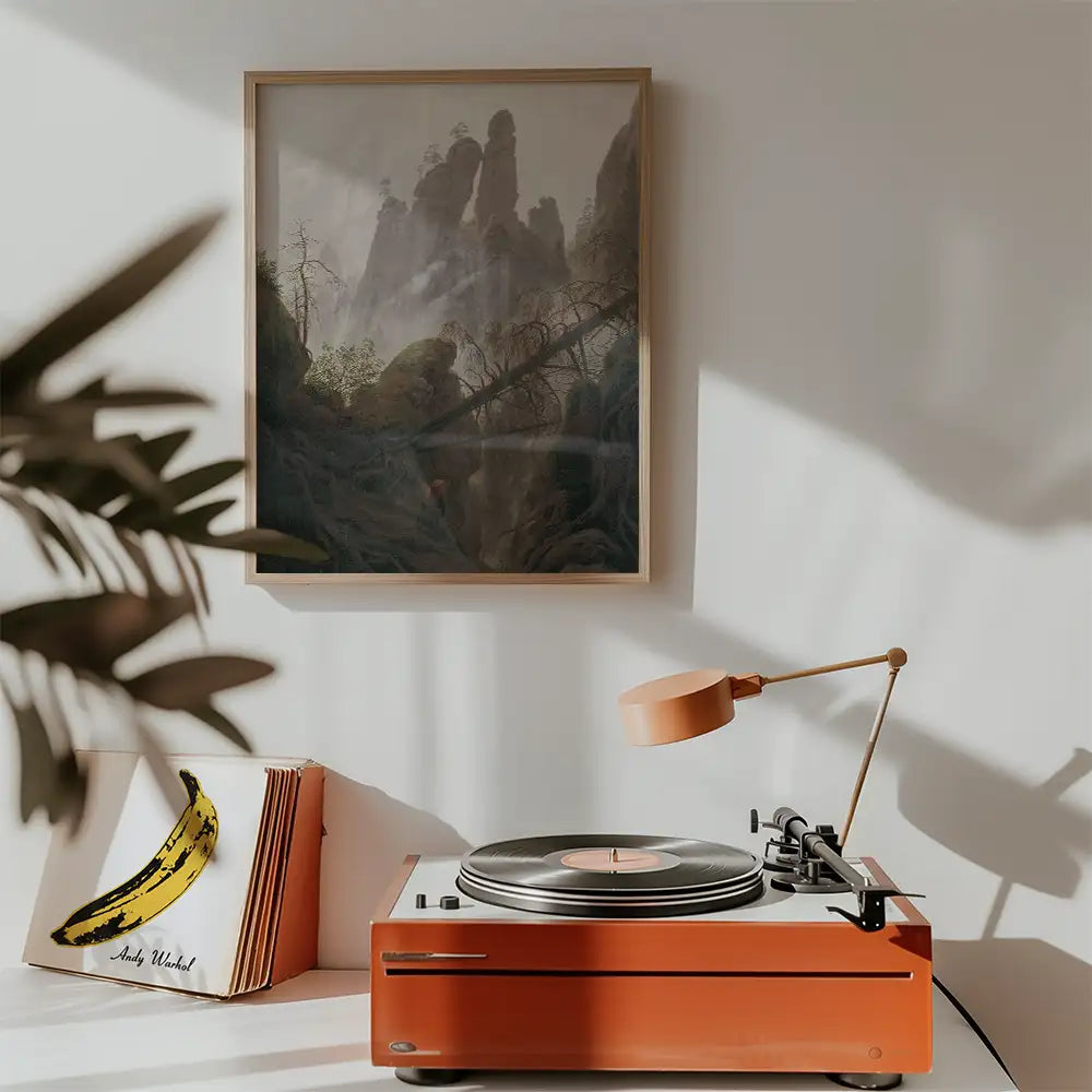 Painting of a serene mountainous landscape in a wooden frame hanging on a wall near a vintage record player and an album cover with a banana design.
