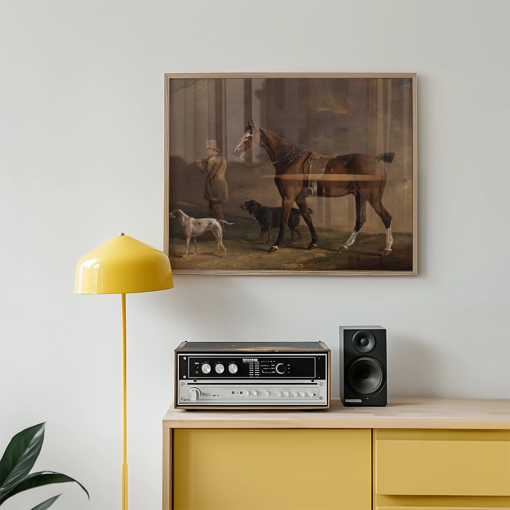 A framed painting of a horse with a rider and two dogs, displayed above a modern yellow lamp and vintage stereo on a wooden sideboard.