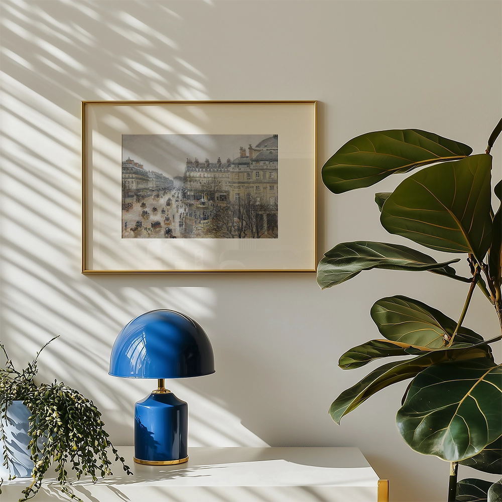 Framed painting of a bustling city street scene, displayed on a light wall alongside a blue table lamp and green plant.