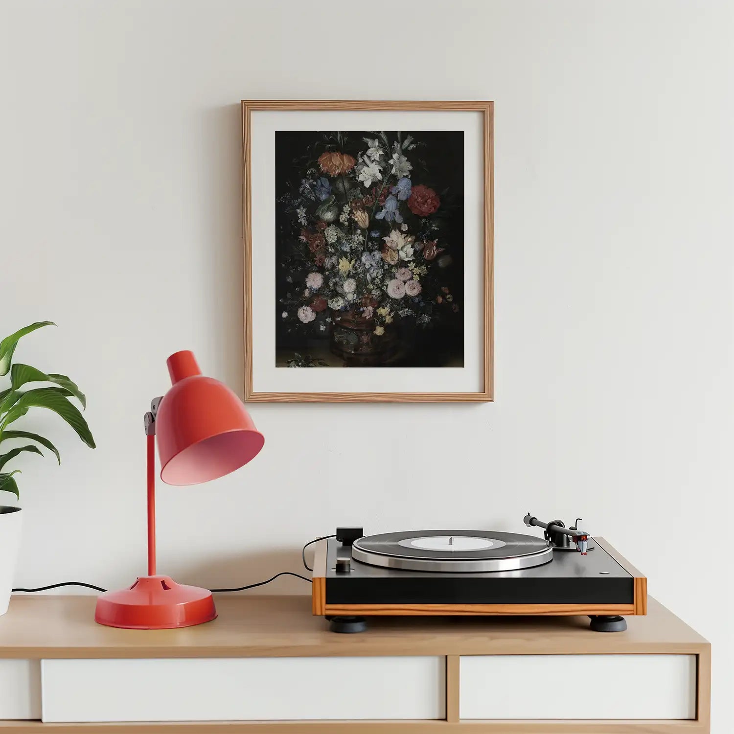 Painting of a floral arrangement in a wooden frame, displayed on a wall above a record player and a red desk lamp.