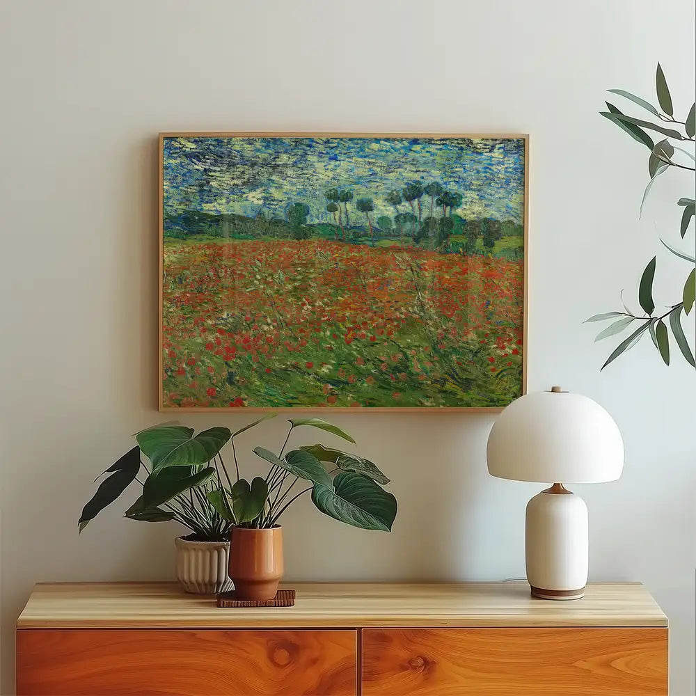 Framed painting of a vibrant field with red flowers under a blue sky, displayed on a light wall above a wooden dresser with potted plants and a lamp.
