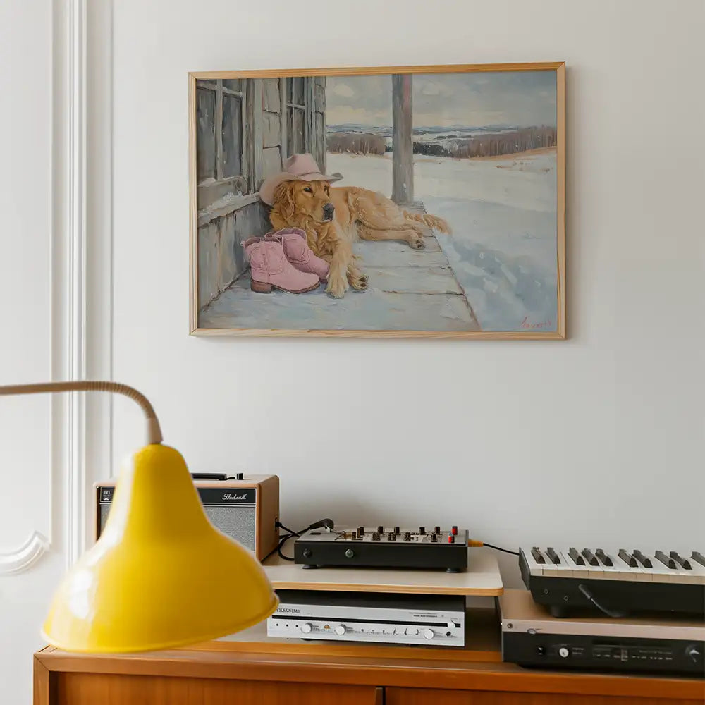 Modern art print of a golden retriever lounging on a porch wearing a pink cowboy hat and sitting next to pink boots, set in a cozy, stylish room with vintage decor.