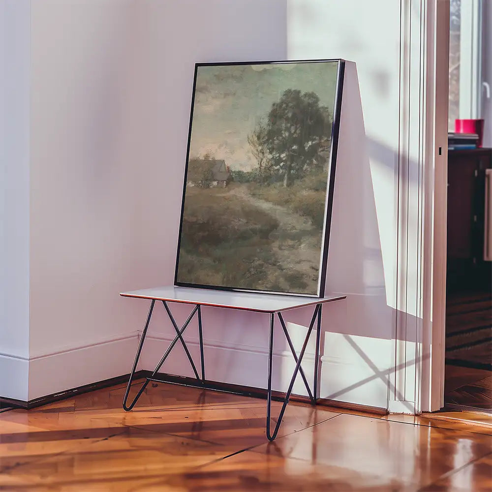 A framed painting of a serene landscape featuring a path and a small house, displayed on a minimalist table in a modern interior setting.