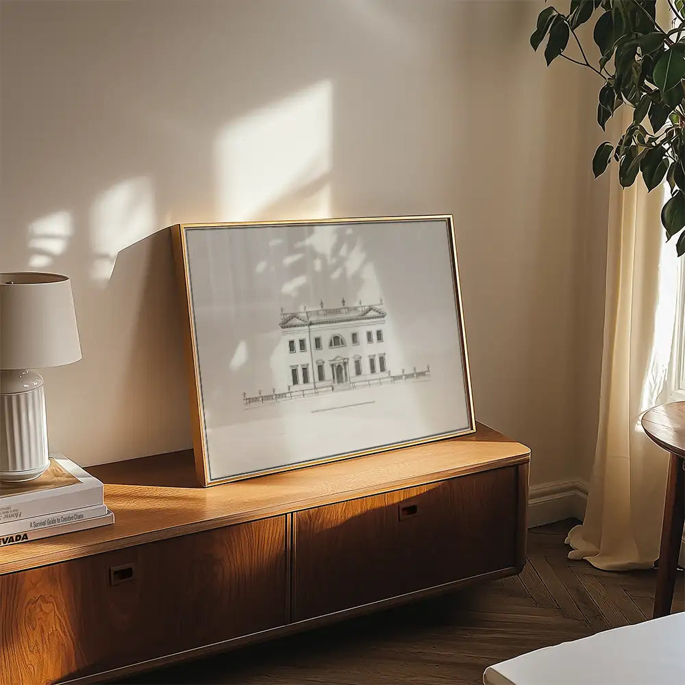 Framed artwork of a classic building displayed on a wooden surface in a well-lit interior setting