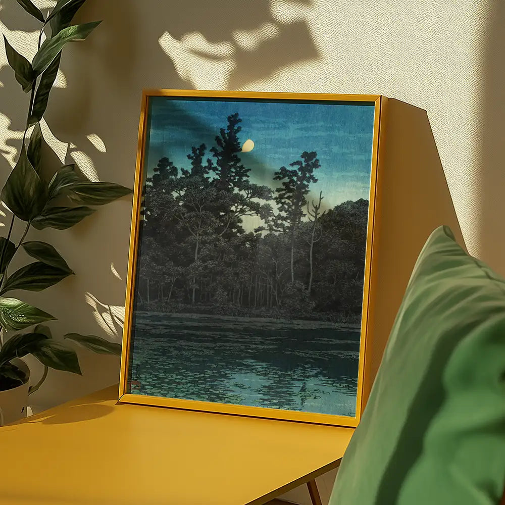 Painting of a serene landscape featuring trees and a moonlit sky, framed in a bright yellow frame, placed on a yellow table with green cushions and plants.