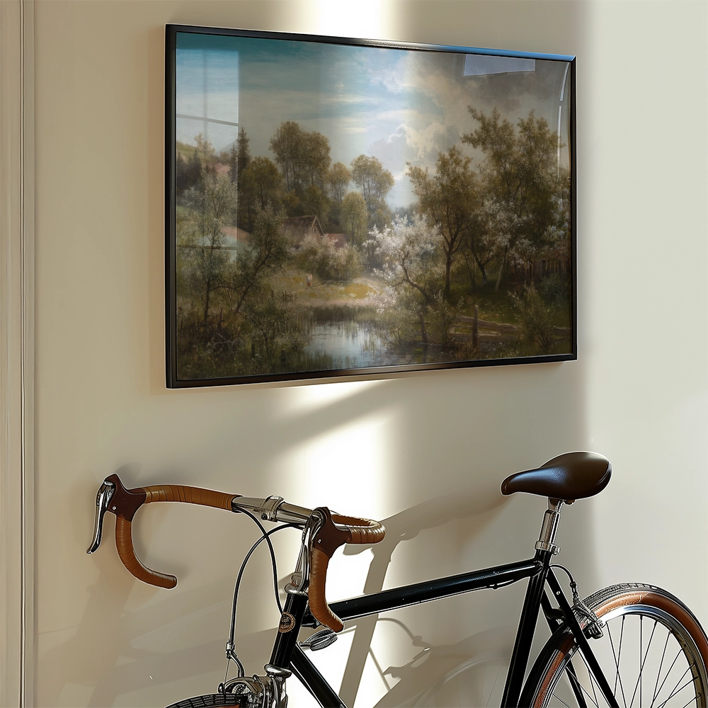 Framed landscape painting depicting a serene scene with trees, a pond, and a bright sky, displayed on a wall next to a vintage bicycle.
