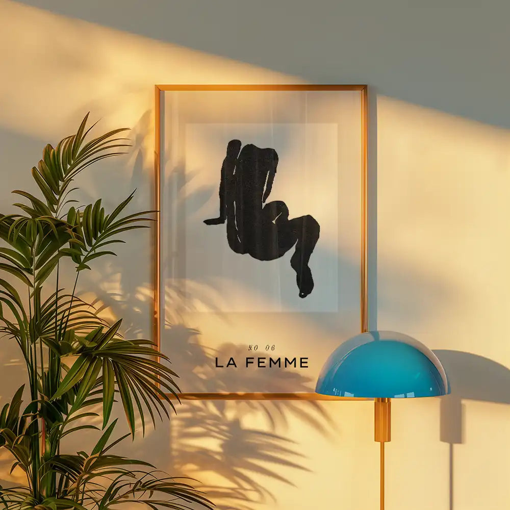 Modern art poster featuring a minimalist black silhouette of a seated woman, framed in gold, with the text "LA FEMME" displayed below, ideal for contemporary home decor.