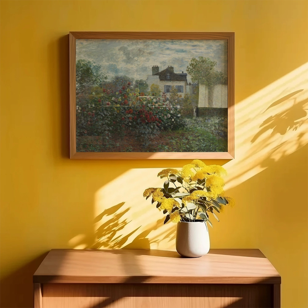 Painting of a floral garden scene in a wooden frame, displayed on a yellow wall above a wooden table with a vase of yellow flowers.