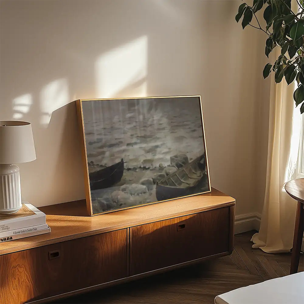 Framed painting of boats on a calm water surface displayed on a wooden table in a cozy interior setting.