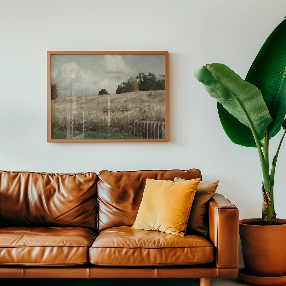 Painting of a serene landscape featuring a grassy field and cloudy sky, framed and hung above a brown leather sofa with pillows and a potted plant.
