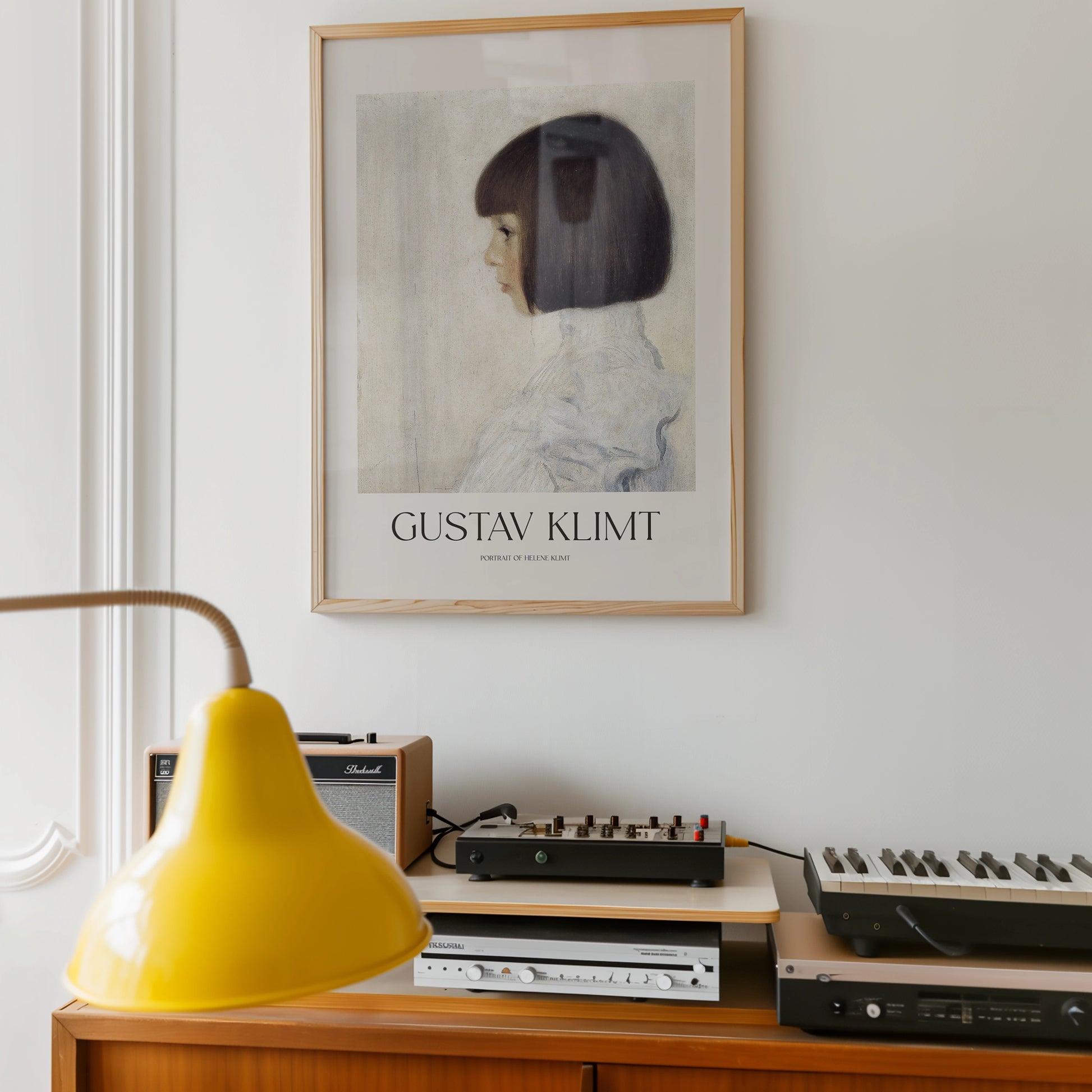 Gustav Klimt portrait poster framed and displayed on a wall above a vintage audio setup with a yellow lamp in the foreground