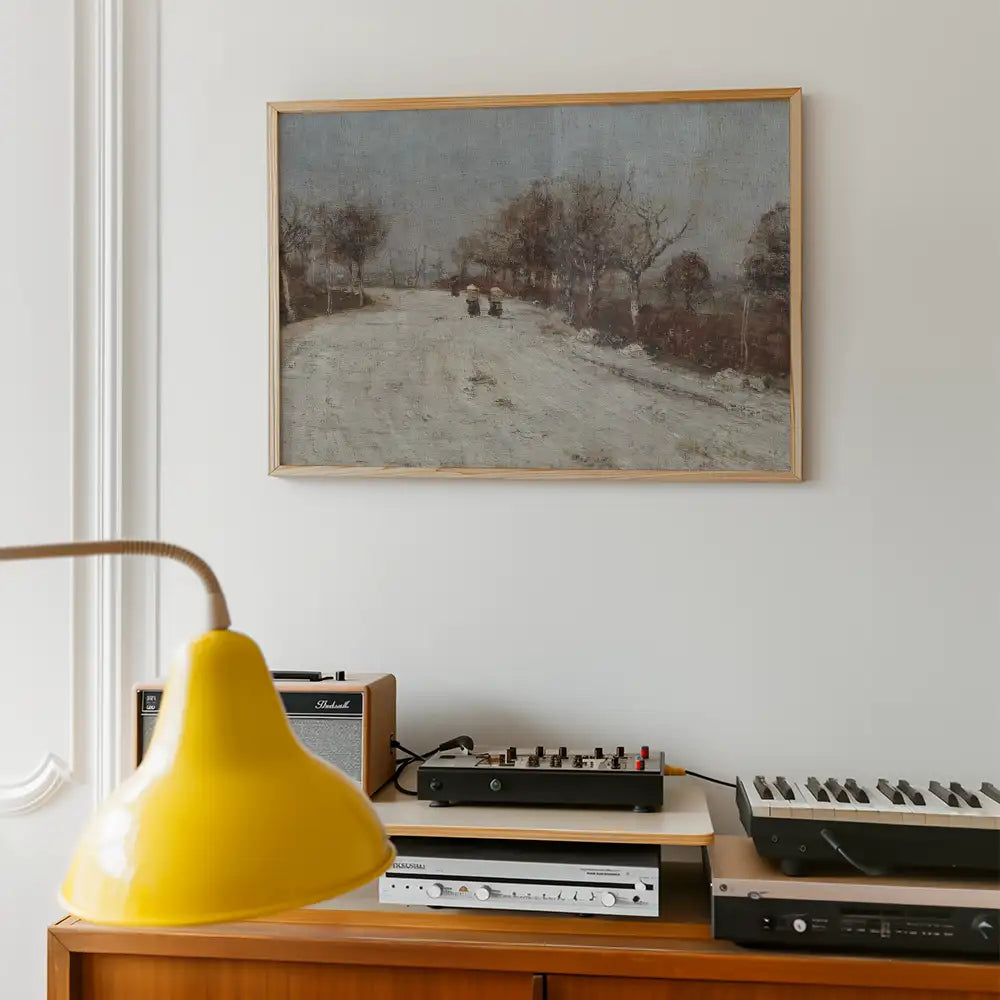 Framed painting of a winter landscape featuring a snowy road and bare trees, displayed on a white wall above a wooden shelf with vintage audio equipment and a yellow lamp.