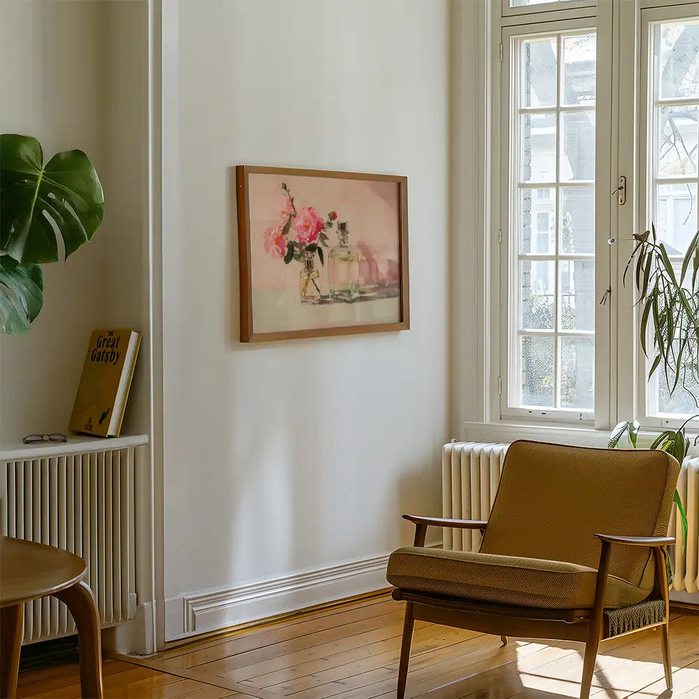 Framed painting of pink flowers on a table displayed in a bright room with a wooden chair and greenery.
