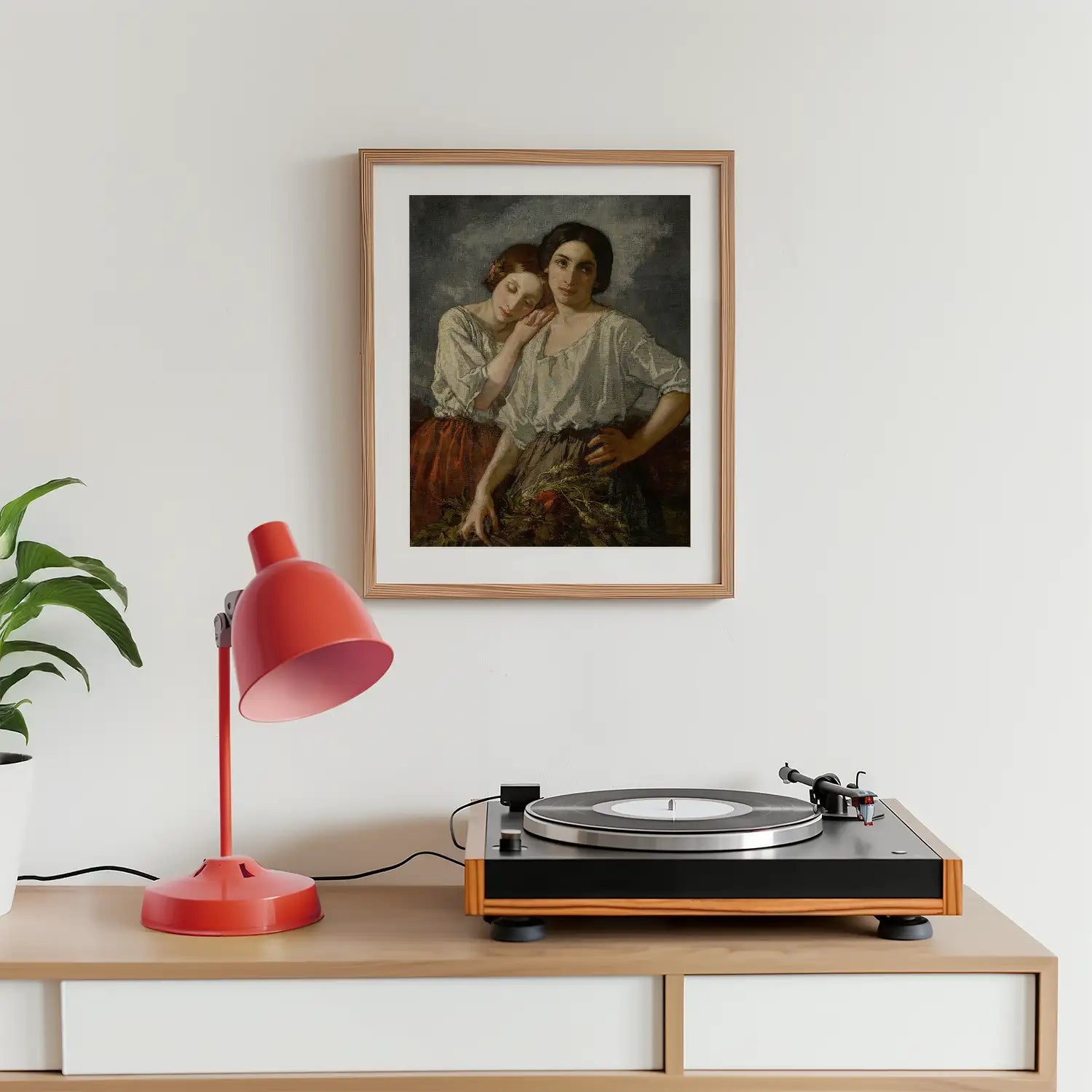 Framed painting of two women in traditional clothing above a record player and a red desk lamp on a wooden surface