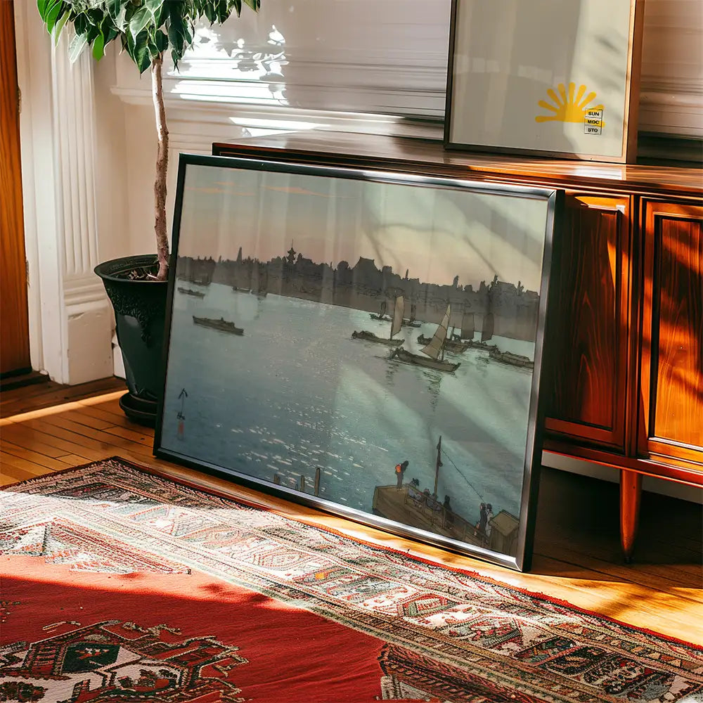 A framed painting depicting boats on a calm river during sunset, leaning against a wooden cabinet in a warmly lit room.