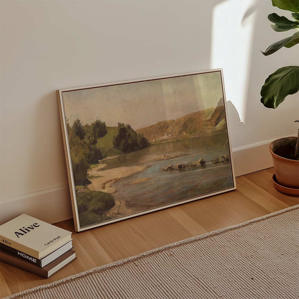 Framed landscape painting resting against a wall beside potted plant and stacked books
