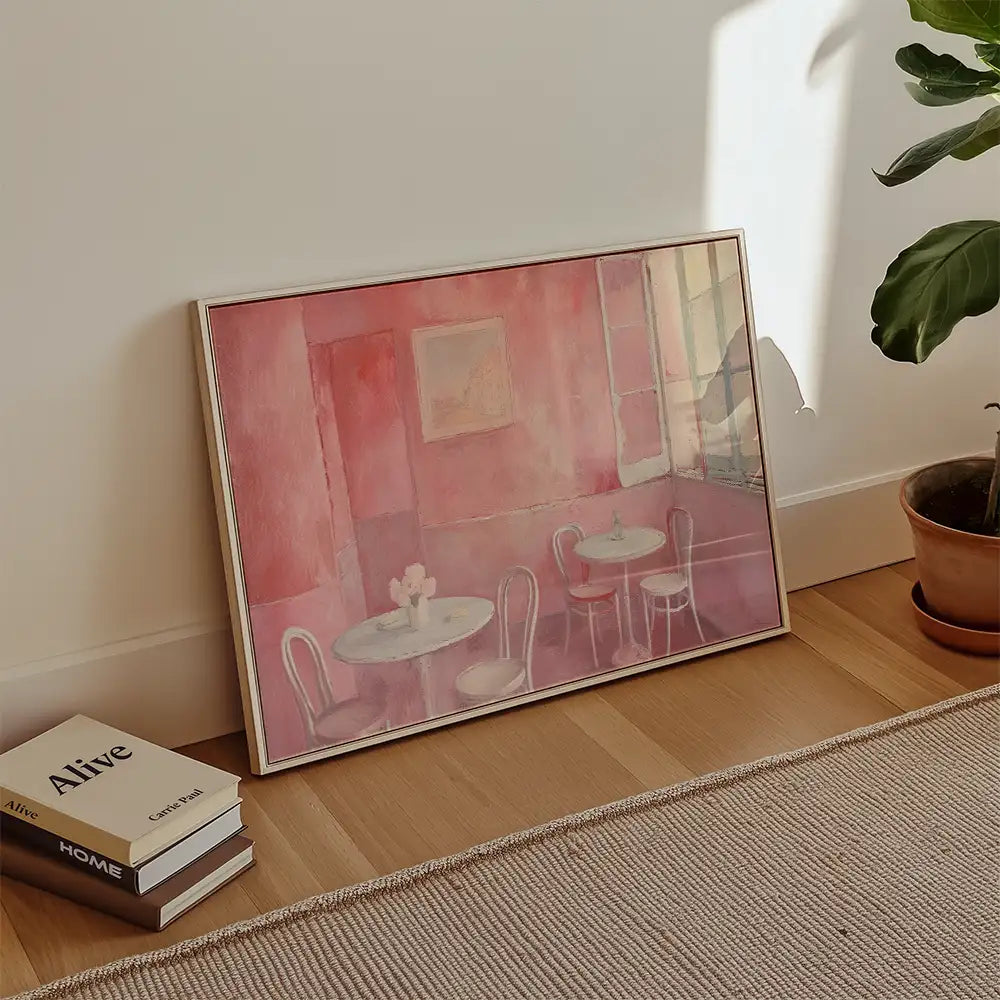 Modern reprint of a famous painting depicting a pink-toned café scene with two tables and chairs, elegantly framed and styled in a contemporary living space.