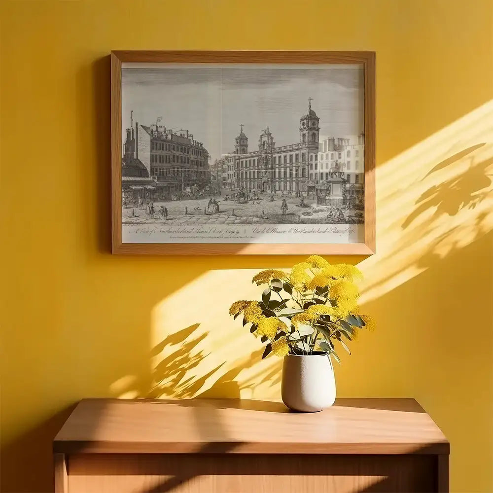 Framed vintage cityscape painting on a yellow wall with a wooden table and a vase of yellow flowers in front.