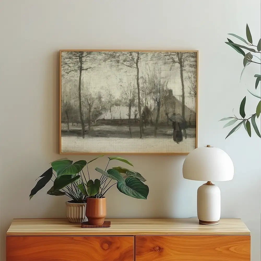Framed black and white painting of a landscape with trees and a house, displayed above a wooden console with a potted plant and a lamp.