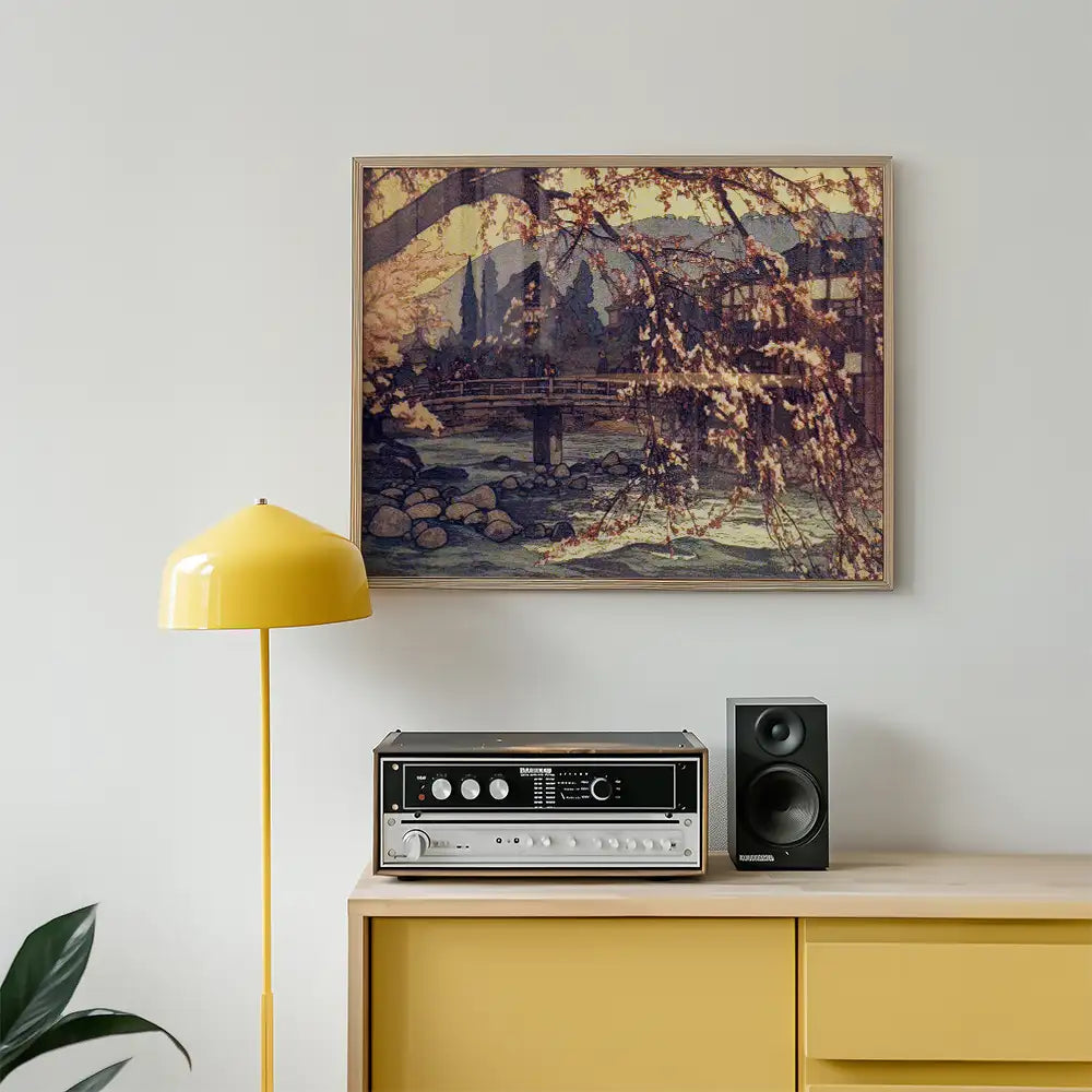 Painting of a serene landscape with a bridge over a stream, framed and displayed above a mid-century modern sideboard featuring a yellow lamp and audio equipment.