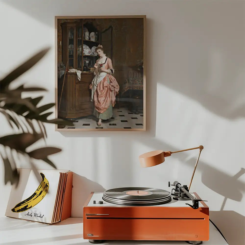 Painting of a woman in a pink dress standing beside a wooden cabinet, framed on the wall above a vintage turntable with an orange casing.