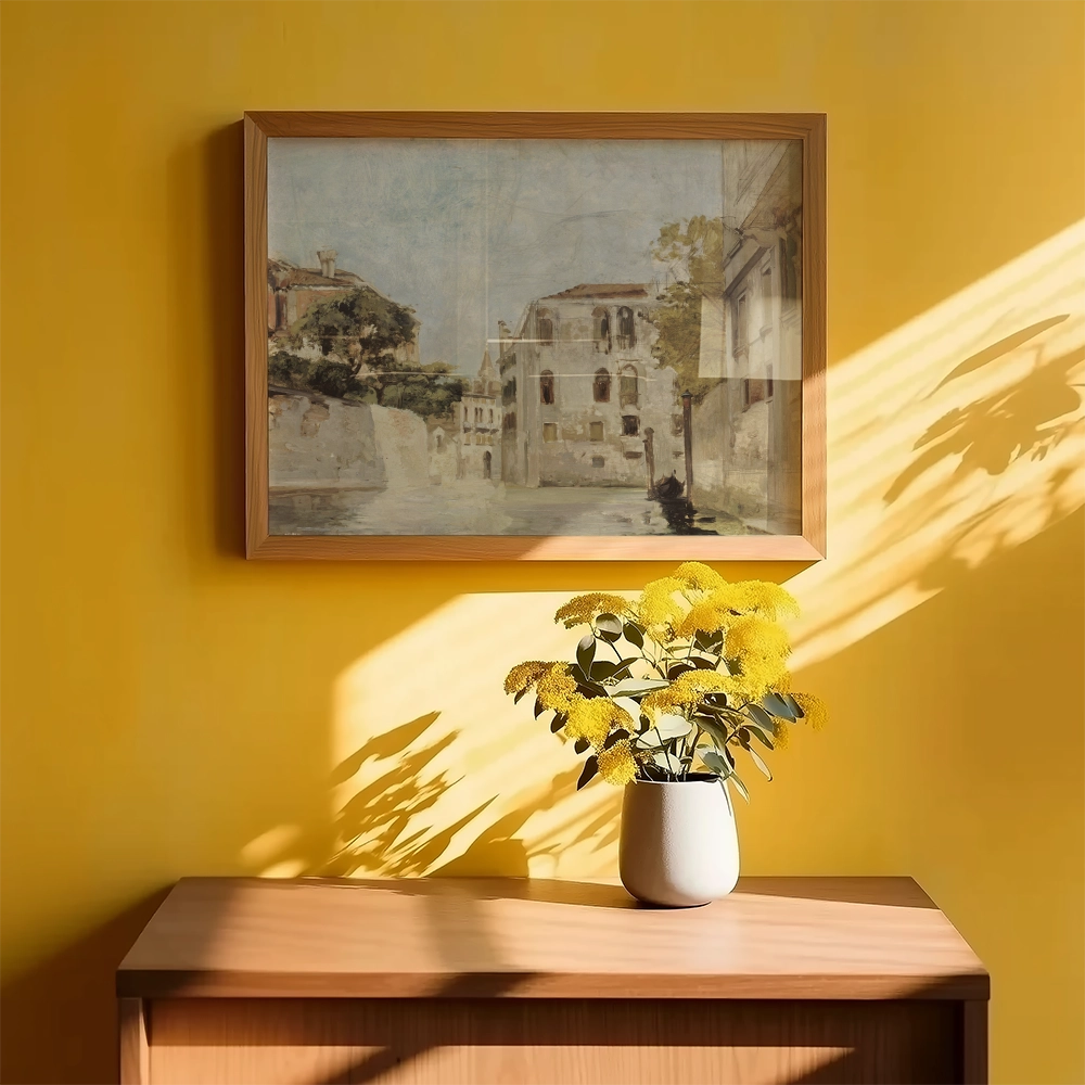 Framed landscape painting on a yellow wall above a wooden cabinet, accompanied by a vase of yellow flowers.