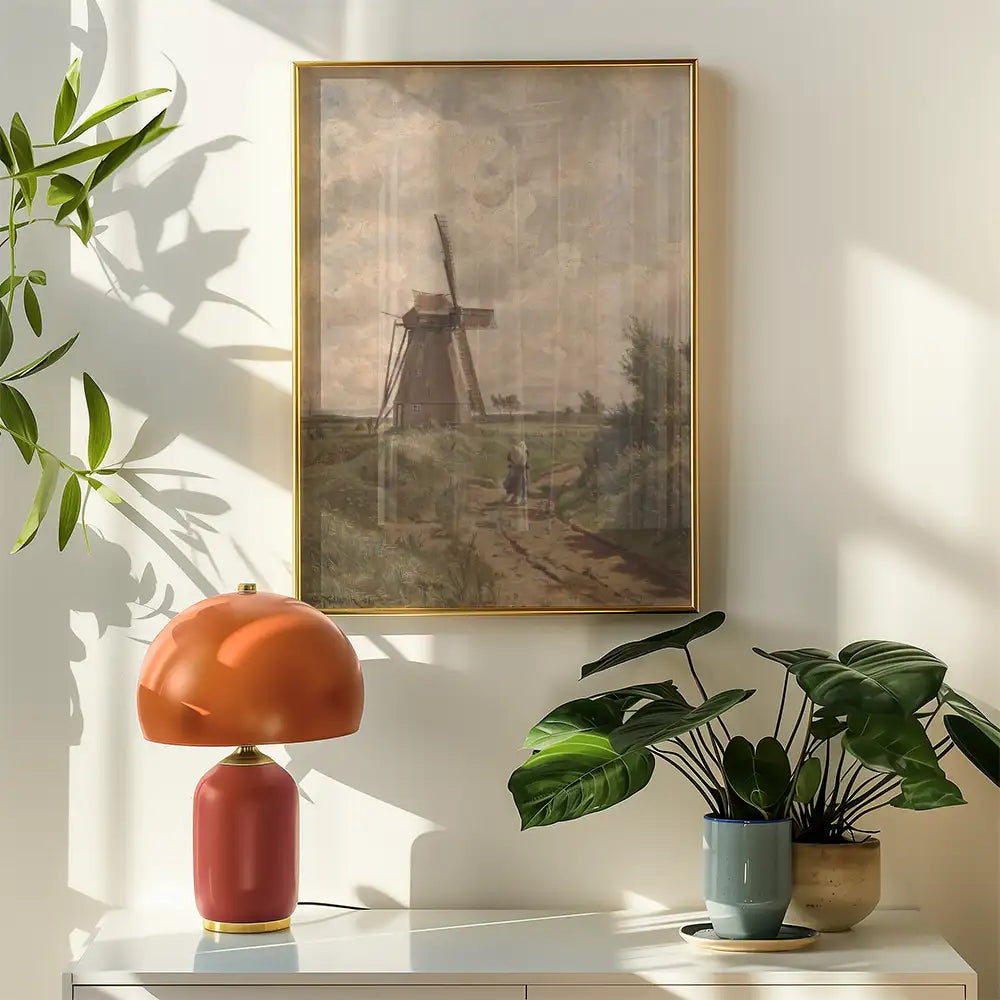 A vintage landscape painting of a windmill framed in gold, displayed on a wall next to a modern orange lamp and potted plants.