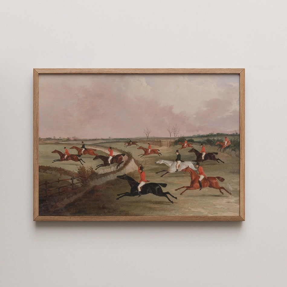 Framed painting of a fox hunting scene with riders in red jackets on horseback, galloping across an open landscape.