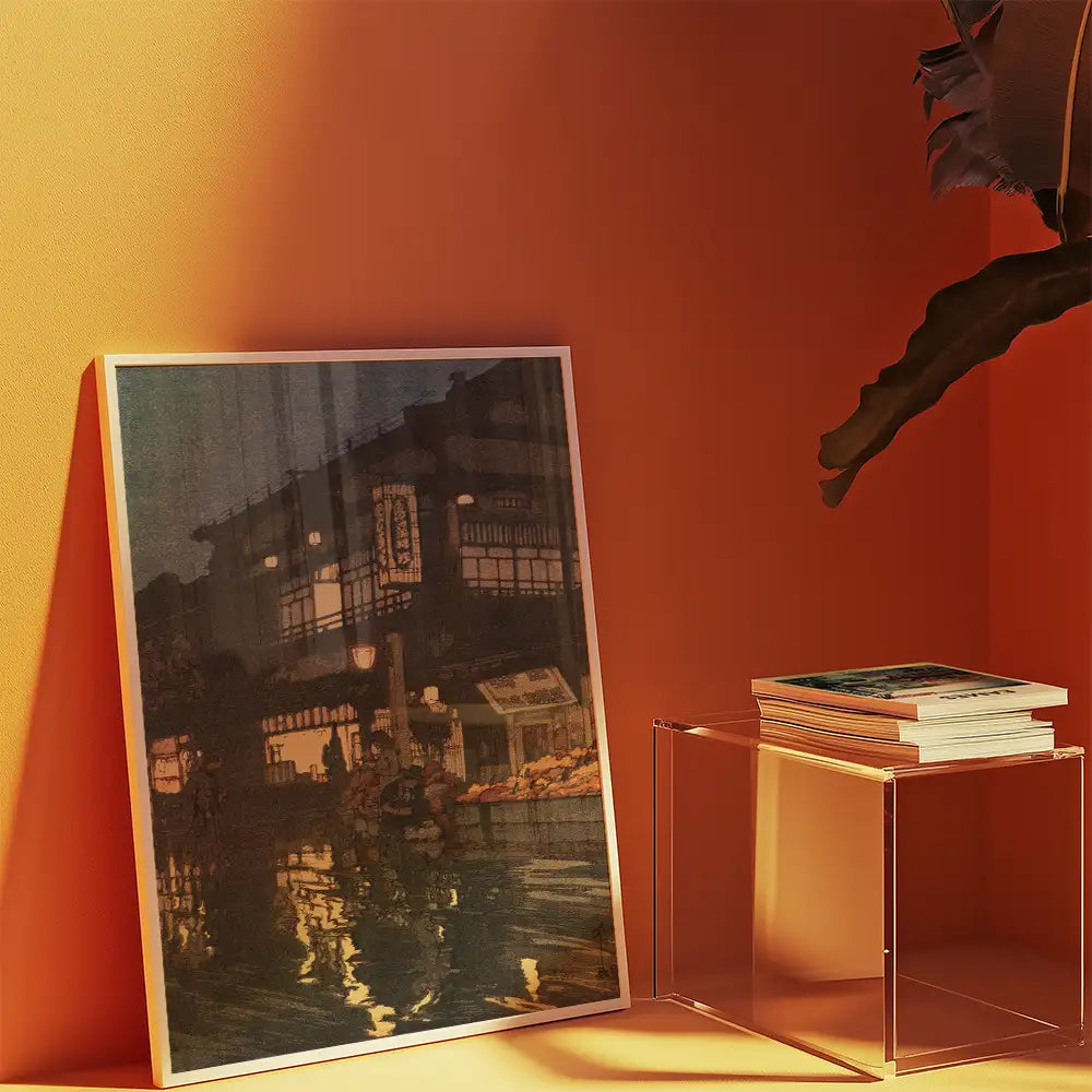 Painting of a nighttime market scene displayed on an orange wall, with a stack of art books on a clear acrylic table beside it.