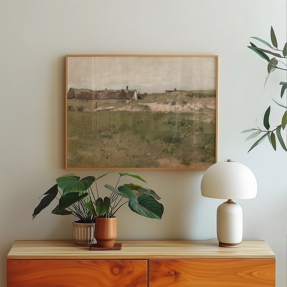 Painting of a landscape featuring grassy fields and distant structures, framed and displayed above a modern wooden sideboard with potted plants and a lamp.
