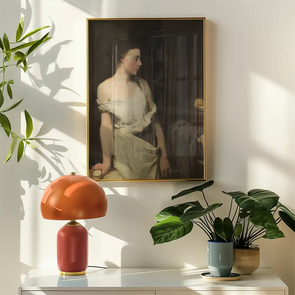 Painting of a woman in soft lighting, framed in gold, hanging above a modern decorative lamp and potted plants on a white surface.