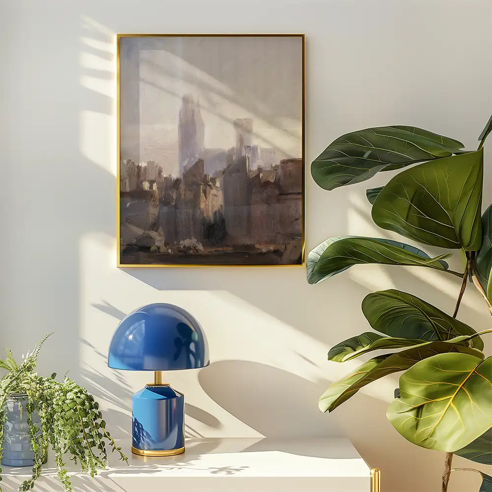 A framed abstract painting of a cityscape hanging on a wall next to a blue table lamp and a large leafy plant.