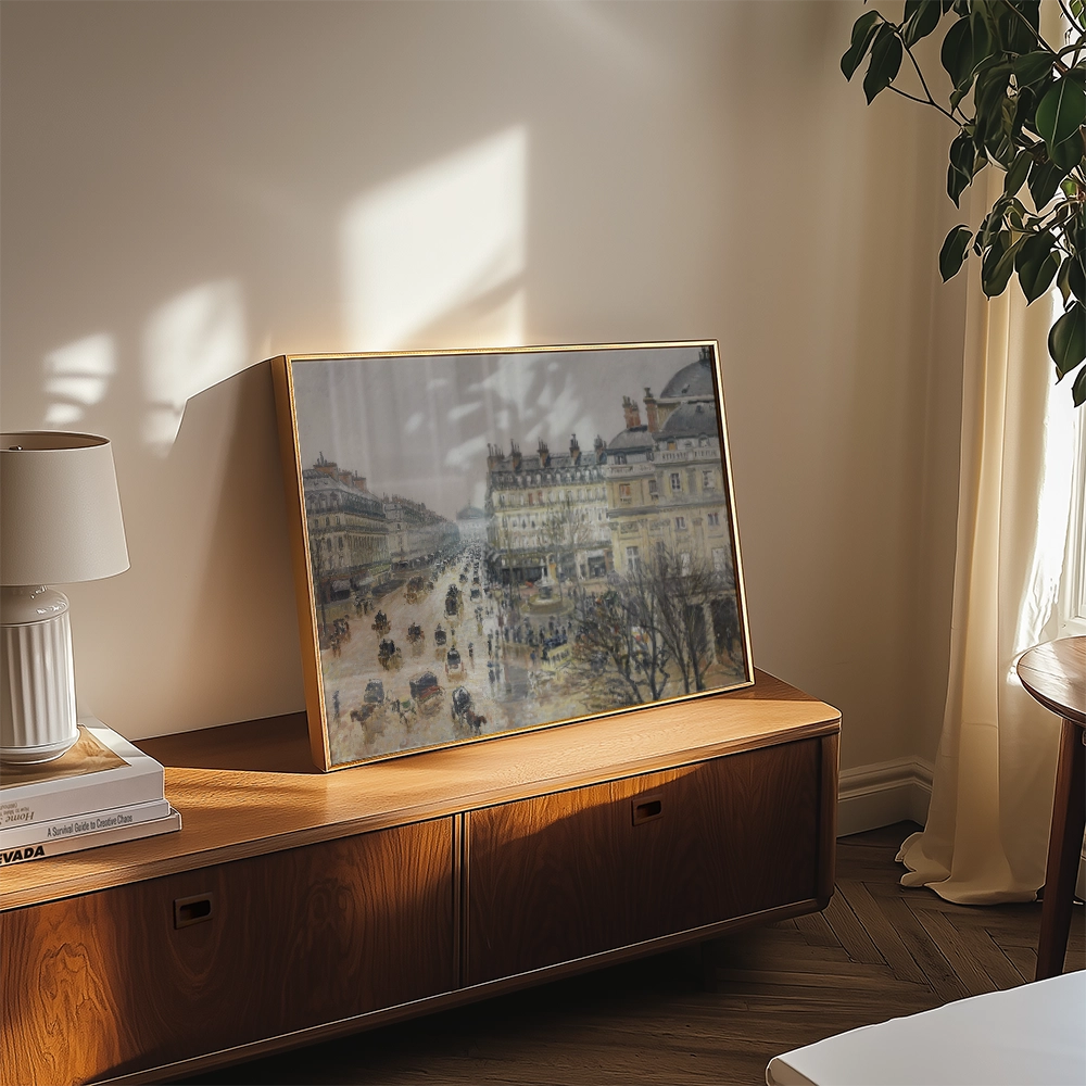 A framed painting of a bustling street scene displayed on a wooden console table in a bright room with natural light.