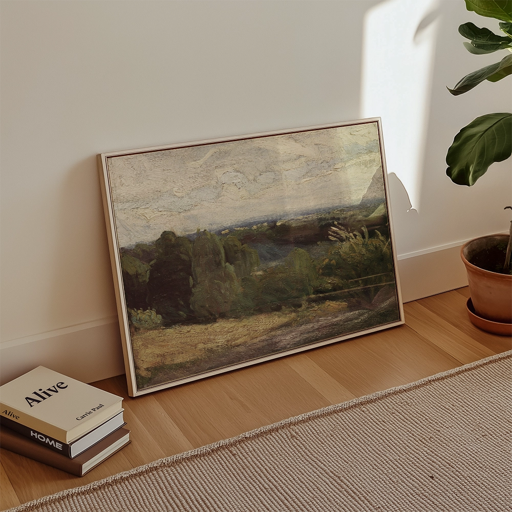 A framed landscape painting propped against a wall with a small potted plant and books on the floor.