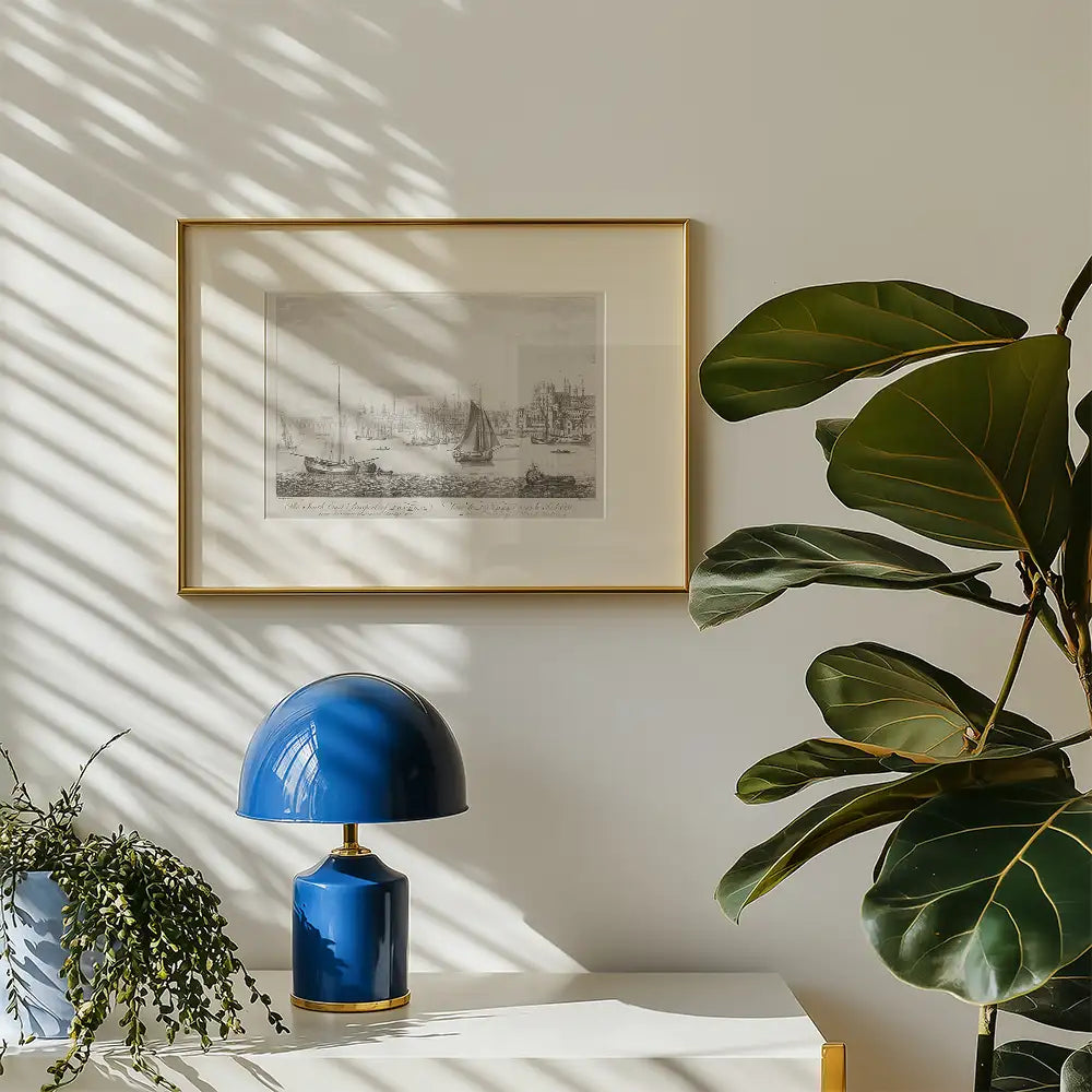 Framed black and white sailing ship artwork on a light wall, accompanied by a blue lamp and a green plant.